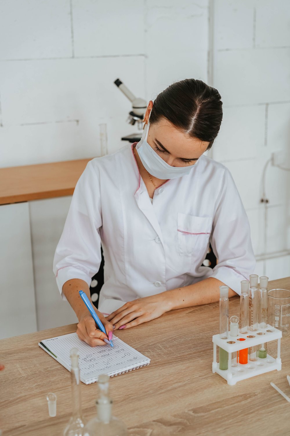 Pracownica laboratorium w maseczce robi notatki przy probówkach
