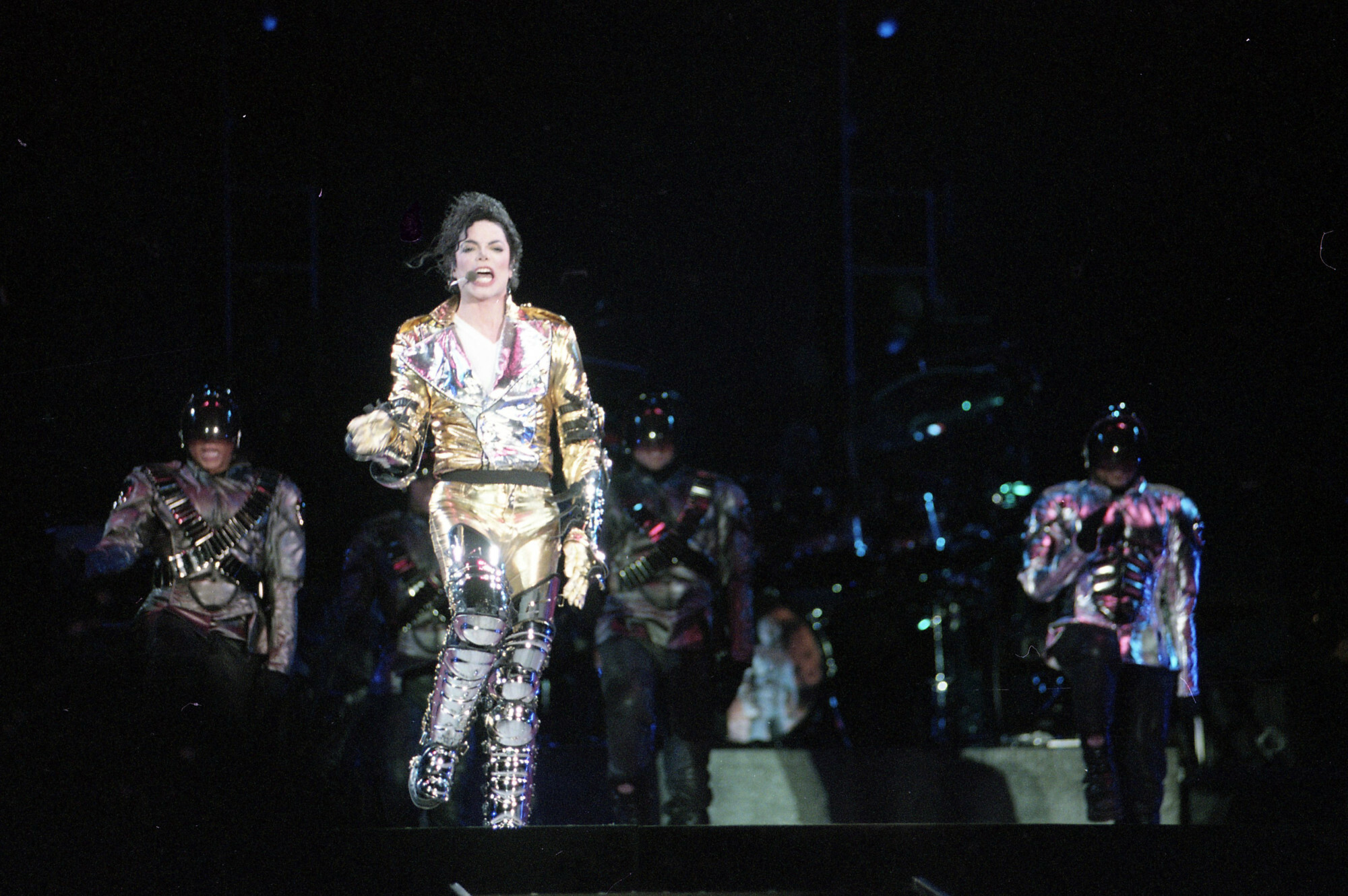 Michael Jackson w złotym kostiumie na scenie, za nim tancerze w hełmach
