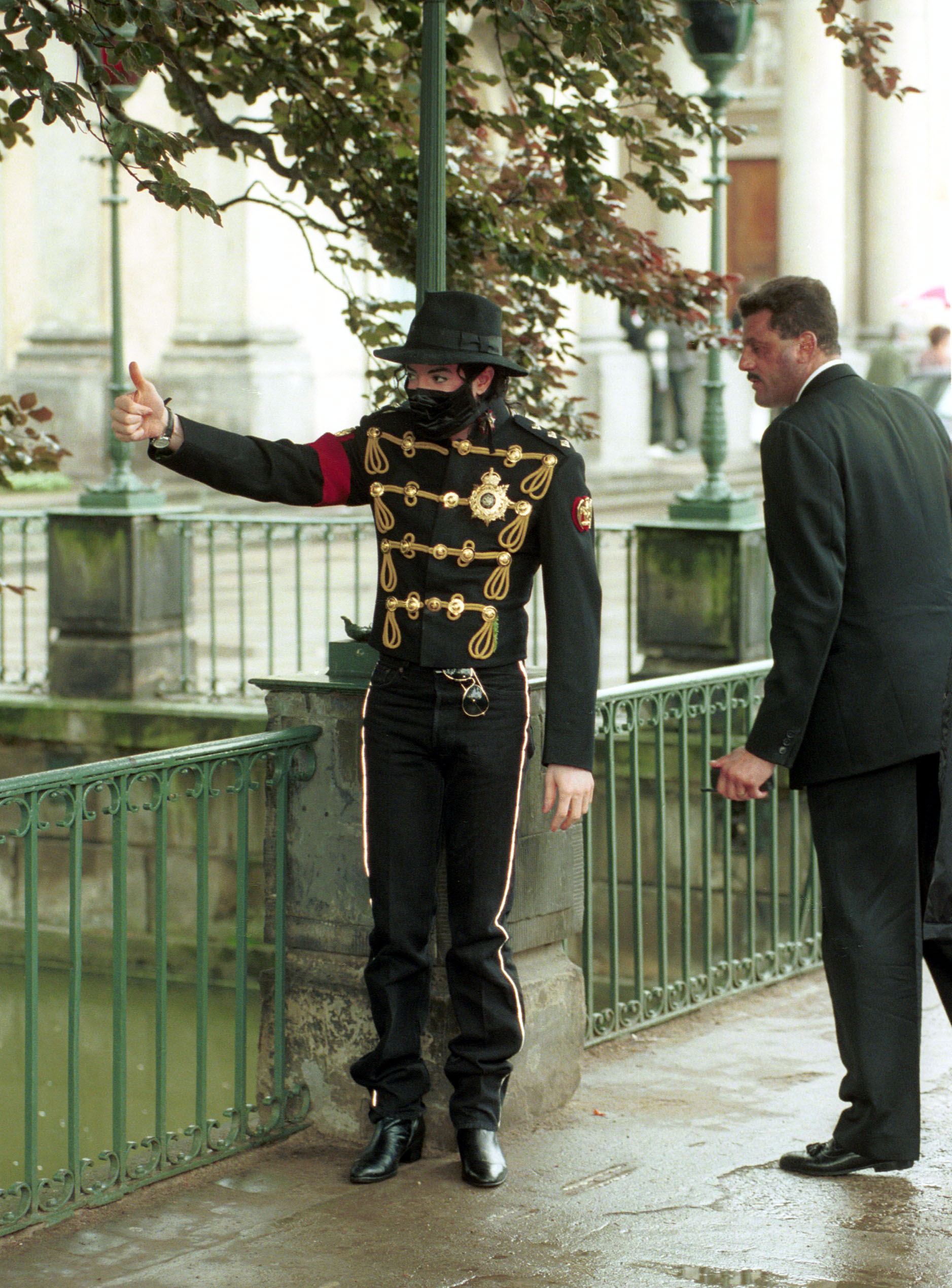Michael Jackson z uniesionym kciukiem przy ogrodzeniu