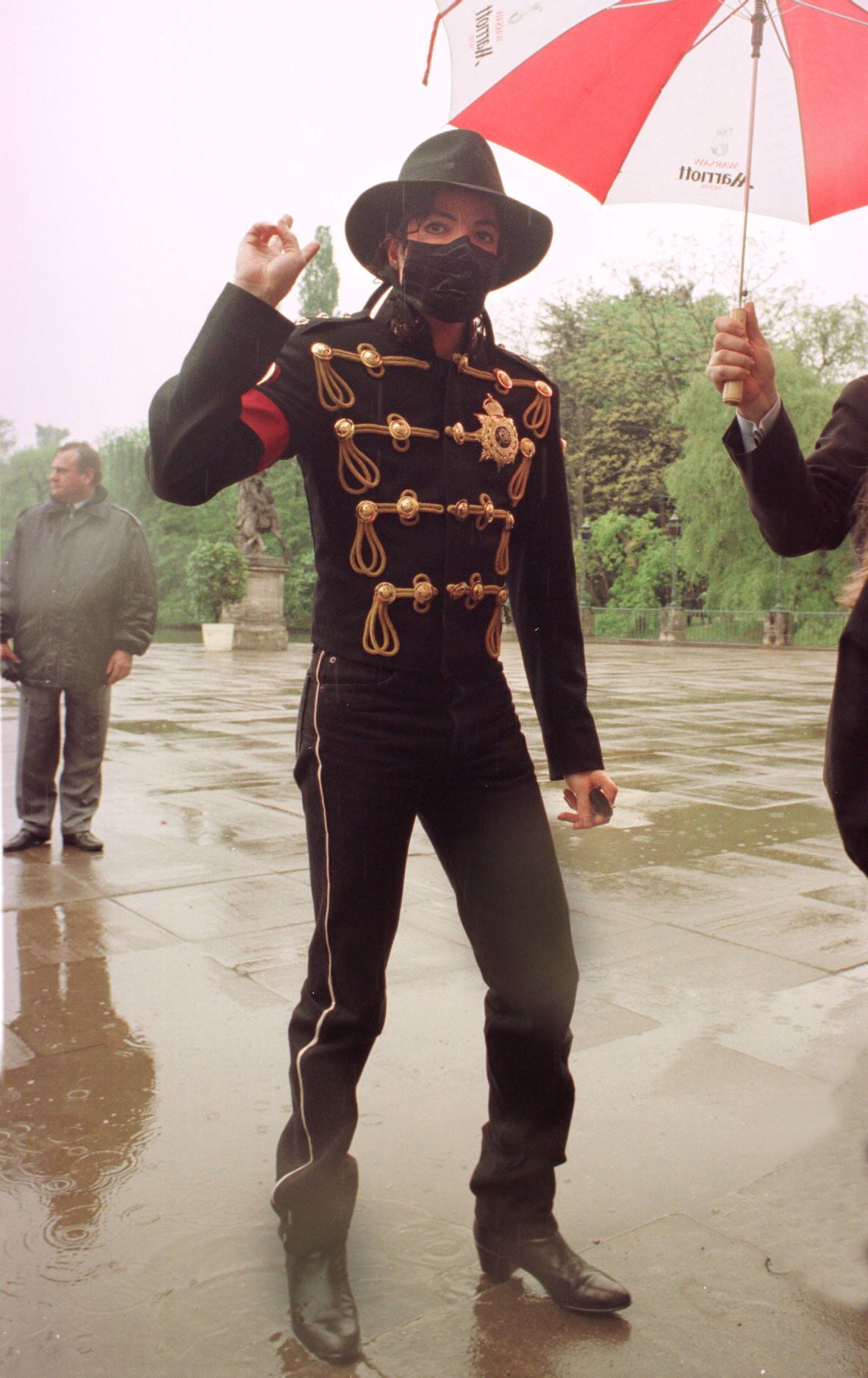 Michael Jackson w deszczu, w czarnym mundurze z czerwoną opaską, ręka uniesiona